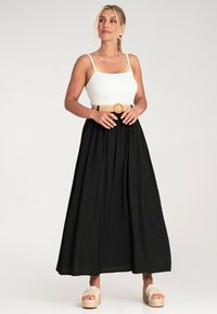 Schwarzer Maxirock mit fließendem Design, kombiniert mit einem weißen gerippten Tanktop und einem strukturierten, hellbraunen Gürtel sowie Plateau-Sandalen.