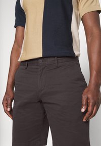 Polo en tricot à manches courtes, de couleur beige, marine et crème ; associé à un short sombre texturé avec fermeture à bouton et poches latérales.