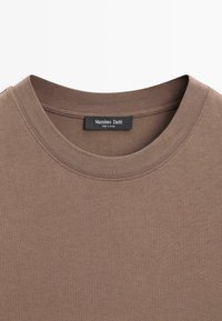 T-shirt di cotone marrone con scollo rotondo, caratterizzata da una texture a coste e un'etichetta con la scritta "Massimo Dutti." Nessun motivo o ornamento visibile.