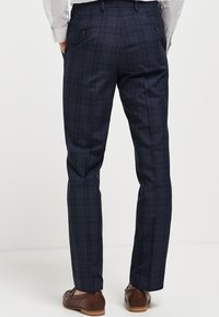 Marine-karierte Hose mit tailliertem Schnitt, seitlichen Eingrifftaschen und hinteren Taschen mit Knopfklappe, aus strukturiertem Stoff mit glatter Oberfläche.
