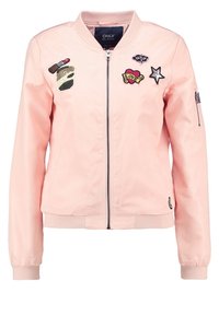 Jasnoróżowa bomberka z gładkiego materiału, ozdobiona naszywkami, w tym gwiazdą, sercem i napisem. Z przodu zamek błyskawiczny i prążkowane mankiety.