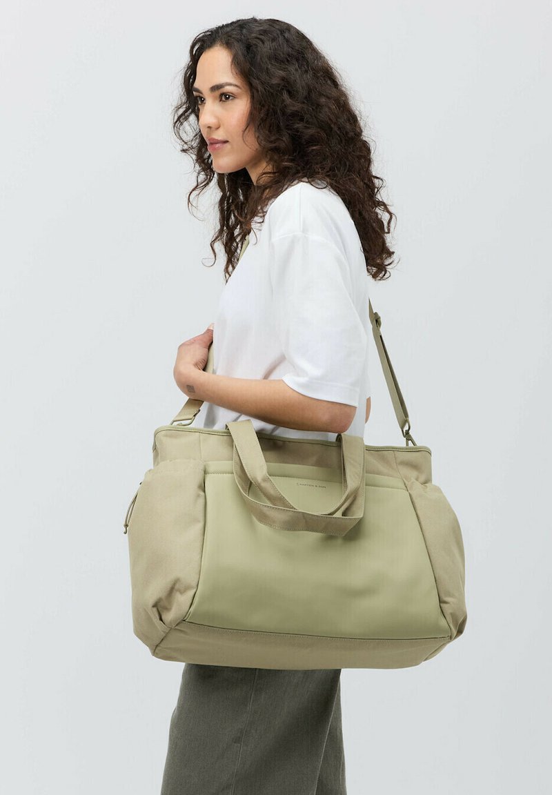 Olive green torba na ramię z dwoma uchwytami i paskiem na ramię. Wykonana z teksturowanej tkaniny z kontrastującą jaśniejszą beżową dolną częścią. Zamek błyskawiczny w kieszeni.