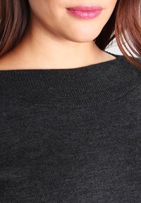 Pull noir en maille avec un large col, une texture douce et un léger éclat. Détail de couture visible autour du col.