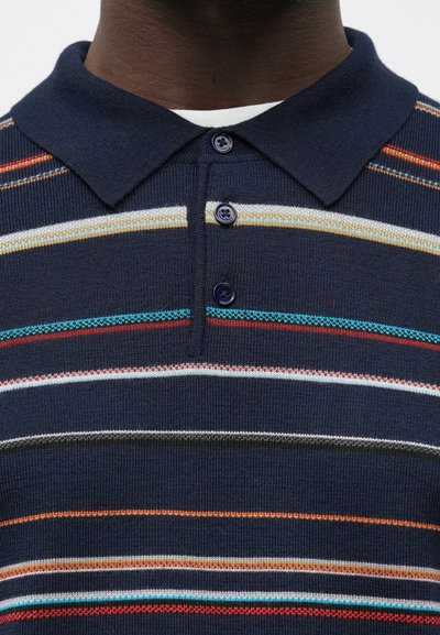 Tmavomodré polo tričko s plochým golierom, s horizontálnymi pruhmi v červenej, oranžovej, bielej a tyrkysovej farbe. Zapínanie na gombíky s tmavými gombíkmi.