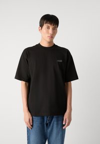 Tricou negru din bumbac cu mâneci scurte, decolteu rotund și logo-ul brodat "BOSS" pe piept. Purtați cu blugi albaștri.