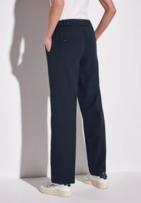 Mörk marinblå, lätta byxor med elastisk midja, sidofickor och avslappnad passform. Slät textur med minimala metalldetaljer.