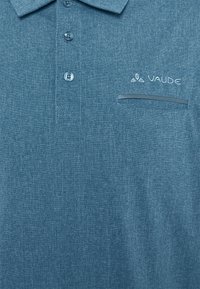 Polo bleu texturé avec trois boutons, une poche poitrine et le logo VAUDE brodé au-dessus de la poche sur le côté droit.