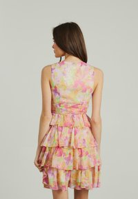Ärmelloses Kleid mit tailliertem Oberteil, geschichtetem Rüschenshirt und einem pastellfarbenen Blumenmuster in Pink, Grün und Gelb. Glatte Stoffoberfläche.
