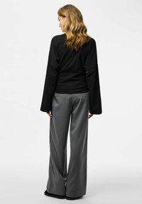 Top nero a manica lunga abbinato a pantaloni grigi a righe sottili a gamba larga, caratterizzati da una vestibilità rilassata e tessuto strutturato. Design semplice, senza motivi visibili.