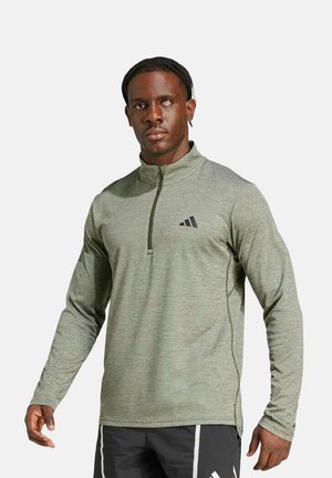 Hombre con discapacidad visual parcial que lleva una sudadera gris claro con cremallera hasta el pecho y pantalones deportivos negros con rayas blancas.