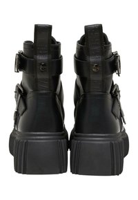 Botas de cuero negras hasta el tobillo con una suela gruesa y texturizada, que cuenta con correas de hebilla y una lengüeta en la parte posterior. Acabado suave y diseño robusto.