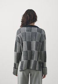 Maglione lavorato a maglia a righe bianche e nere, caratterizzato da una vestibilità ampia, maniche lunghe e colletto rotondo. Motivo testurizzato su tutta la superficie.