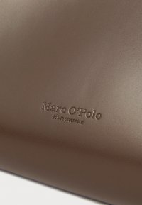 Rjava usnjena denarnica z vtisnjenim logotipom "Marc O'Polo" in napisom "est. v Stockholmu", gladka tekstura z minimalističnim dizajnom.