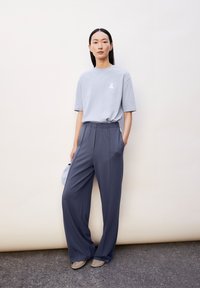 Lichtgrijze t-shirt met een klein wit logo, gecombineerd met donkergrijze wijde broek. Gelukkig stof met een elastische tailleband. Minimalistisch ontwerp.