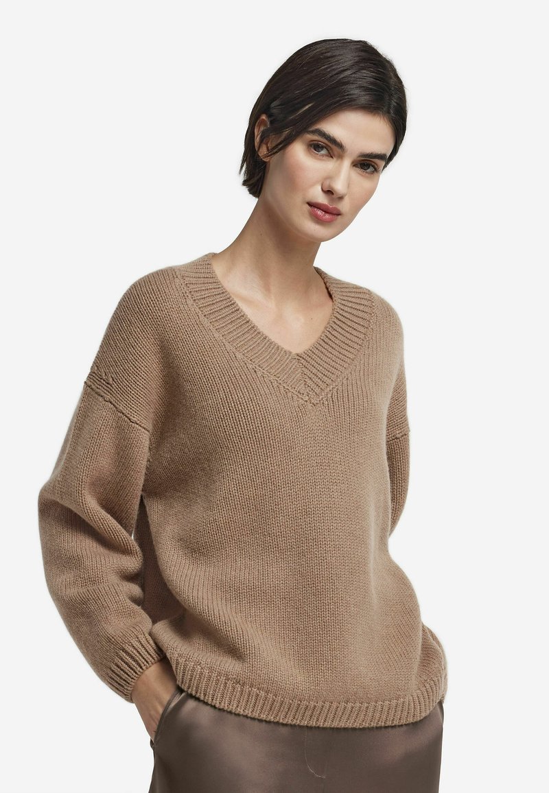 Pull beige en tricot avec encolure en V, coupe ample et poignets et ourlet côtelés. Texture douce et design décontracté idéal pour être superposé.