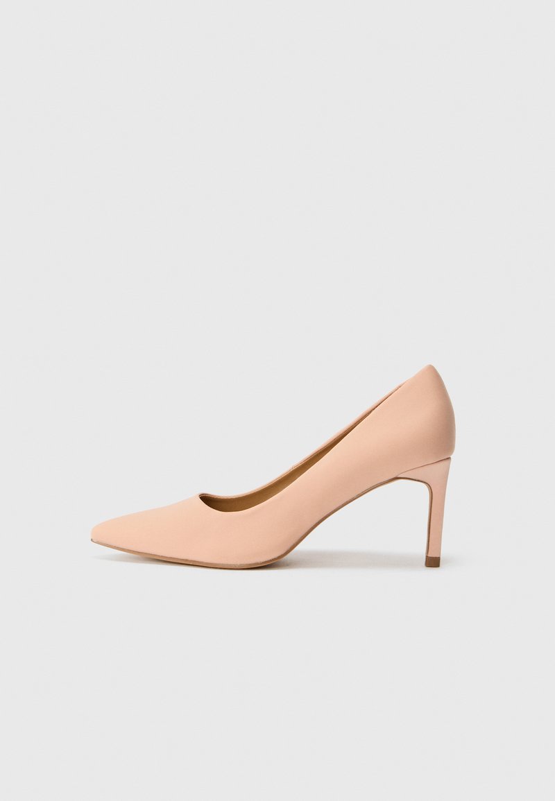 Nude spiss tå pumpe laget av glatt materiale, med en elegant silhuett og en slank stilettohæl. Lett buet bakdesign.