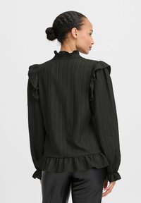 Blusa a righe nere con spalle e polsini a volant, caratterizzata da un orlo volant. Realizzata in tessuto leggero con una texture liscia.
