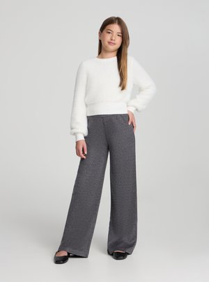 Maglione bianco e soffice con polsini a coste, abbinato a pantaloni grigio scuro testurizzati, a vita alta e dalla vestibilità ampia, e scarpe basse nere.