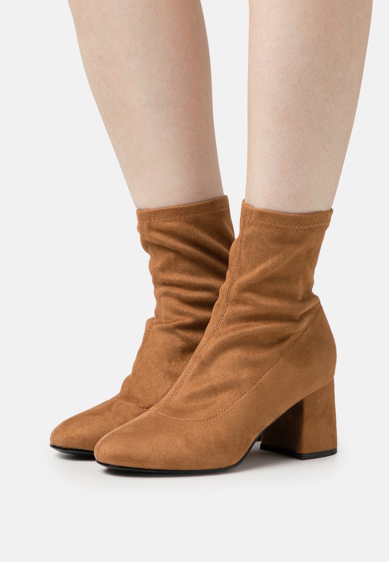 Bottines en daim marron à design décontracté, bout pointu et talon épais. La texture est lisse avec des accents de coutures visibles.