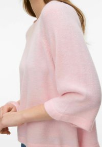 Svetlo roza pulover s tremi četrtinskimi rokavi, mehke teksture, z okroglim izrezom in sproščenim krojem, zasnovan brez vidnih zapenjanj.