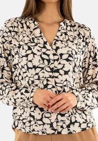 Blusa de manga larga hecha de tejido arrugado, con un patrón floral en negro y crema y cierres de botones en la parte frontal.