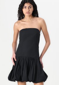 Robe noire sans bretelles en tissu lisse. Corsage ajusté avec une jupe évasée froncée qui a une forme de ballon. Aucun embellissement visible.