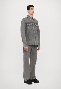 Gray denim jacket and pants set, featuring a button-up closure, two chest pockets, and a slightly textured finish. Black shoes complete the outfit.