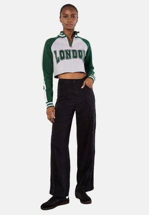 Grau und grün beschnittenes Sweatshirt mit "LONDON" Druck, Reißverschlusskragen, langen Ärmeln, kombiniert mit schwarzen, weiten Cargo-Hosen und dunklen Sneakers.
