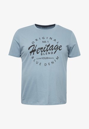 Lichtblauwe katoenen t-shirt met korte mouwen, ronde hals en zwarte bedrukte tekst met "Heritage Blend" en "Blue Denim" op de voorkant.