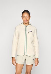 Kreemikas fleece jope, millel on lukuga eesmine osa, kapuuts ja roheline äär. Omab kahte külgtaskut ja väikest logo rinnal. Pehme tekstuur.