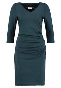 Robe bleu sarcelle foncé arrivant aux genoux, manches trois-quarts, encolure en V, avec un léger froncé sur le côté, sur fond blanc.