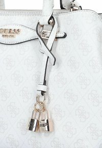 Sac à main en synthétique blanc avec une finition texturée, des bords noirs, des éléments en or, et deux serrures décoratives attachées à un détail en forme de nœud.