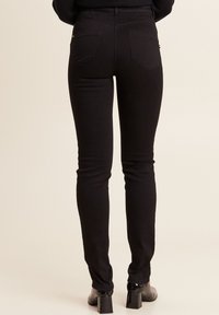 Jeans skinny neri realizzati in tessuto elasticizzato, con un alto punto vita, due tasche posteriori e una finitura liscia. Abbinati a stivali neri con tacco.