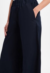 Donkerblauwe, wijde broek met een elastische tailleband en zijzakken, gemaakt van een gladde, lichte stof. Geen zichtbare patronen.