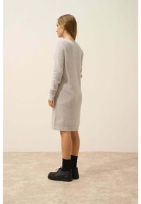 Abito in maglia grigio con maniche lunghe, texture a coste e design al ginocchio, abbinato a scarpe nere e calzini.