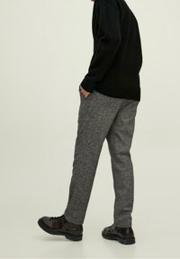 Pantalon gris texturé associé à un pull en maille noire et des bottes foncées, présentant une coupe décontractée et des poches avant visibles.