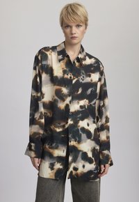 Camicia a maniche lunghe con un motivo astratto in nero, marrone e crema, con chiusura a bottoni sul davanti, realizzata in un tessuto liscio e lucido.
