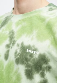 Ανοιχτό πράσινο φούτερ με tie-dye σχέδιο, διαθέτει στρογγυλή λαιμόκοψη και λευκό λογότυπο "huf" στο στήθος. Μαλακό ύφασμα με υφή.
