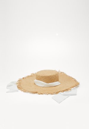 Leveälierinen, punotusta oljesta valmistettu hattu, jossa on kuluneet reunat ja valkoinen kangasnauha, joka on solmittu löysiin rusettiin valkoisella taustalla.