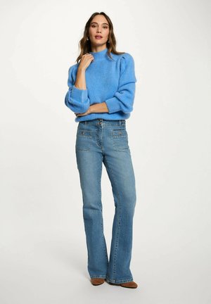 Maglione blu lavorato a maglia con collo alto e maniche a sbuffo abbinato a jeans chiari a palazzo. L'outfit presenta una vestibilità comoda e un design semplice.