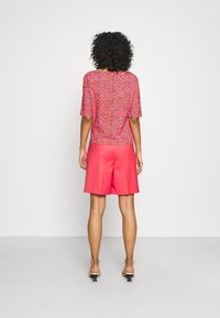 Růžový top s květinovým vzorem a krátkými rukávy v kombinaci s jednobarevnými růžovými šortkami. Model má na sobě světlé sandály na podpatku.