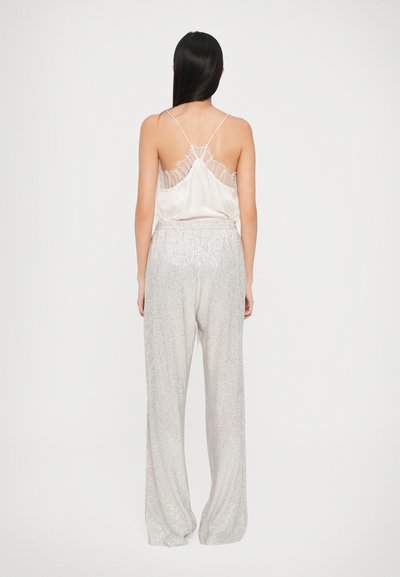 Camisă din satin crem cu detalii din dantelă la spate, asociată cu pantaloni largi din paiete argintii. Textură netedă, design elegant.