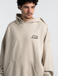 Hoodie beige realizzato in morbido tessuto, con una grande tasca a canguro e un piccolo logo sul petto. Vestibilità rilassata con cappuccio regolabile.