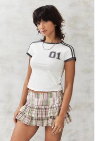 Weißes kurzärmliges Cropped-Top mit grauen Akzenten und "01"-Druck, kombiniert mit einem pastellfarbenen, karierte Rüschenskel mit rosa, grünen und weißen Tönen.