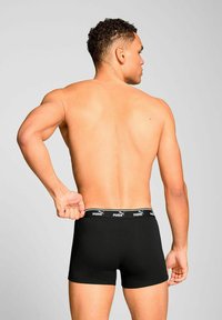 Black boxer briefs made of smooth fabric, featuring a wide elastic waistband with white branding. Designed for a snug fit.