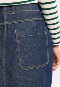 Jupe en denim foncé avec une poche arrière et des coutures contrastées. Le tissu a une texture lisse et est mis en valeur par une chemise à rayures.