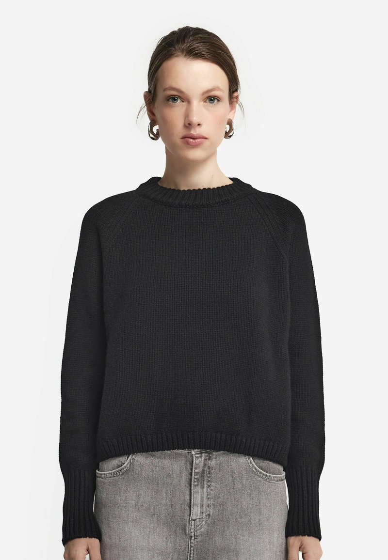 Svart stickad tröja med rund hals, ribbade ärmslut och nederkant. Har en avslappnad passform och strukturerad tyg, matchad med grå denimbyxor.