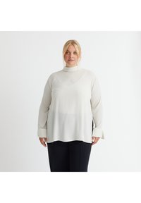 Weiße Bluse mit langen Ärmeln und hohem Kragen, hergestellt aus einem glatten, leichten Stoff. Verfügt über eine lockere Passform und geknopfete Ärmel.