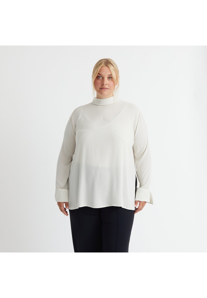 Weiße Bluse mit langen Ärmeln und hohem Kragen, hergestellt aus einem glatten, leichten Stoff. Verfügt über eine lockere Passform und geknopfete Ärmel.