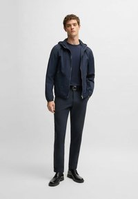 Navy waterproof jacket with hood, paired with a fitted navy shirt and slim trousers. Black leather shoes complete the look.